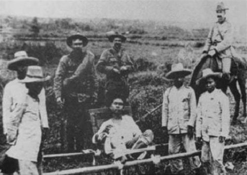 A man on a hammock (presumably Apolinario Mabini) guarded by Americans